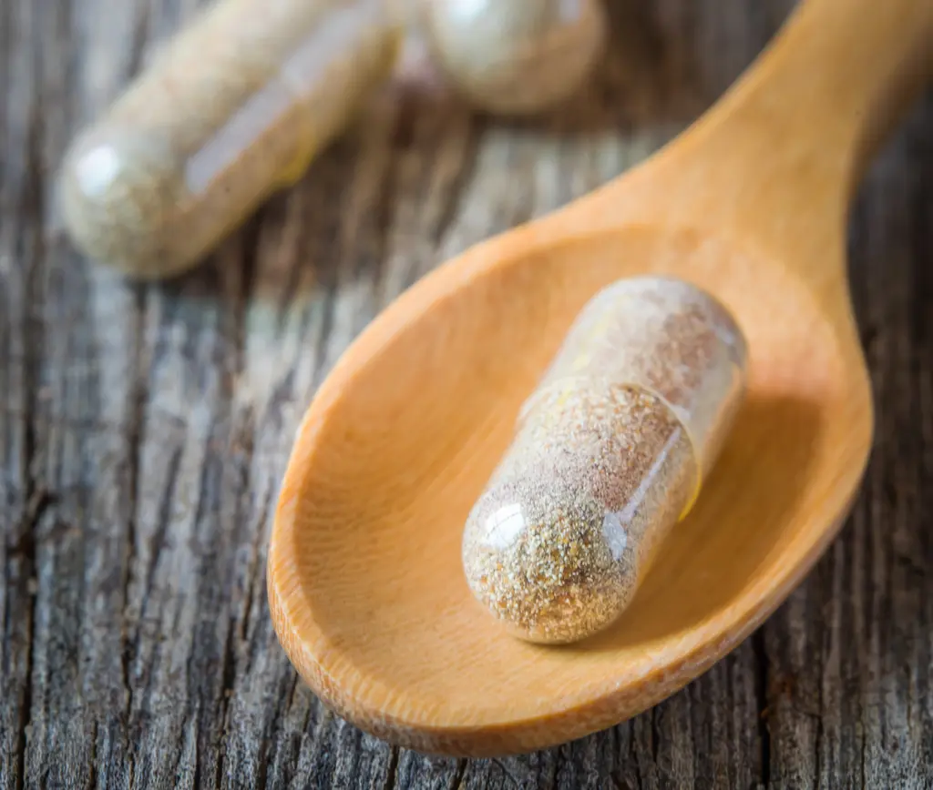 Herb capsules spilling in wooden spoon.
